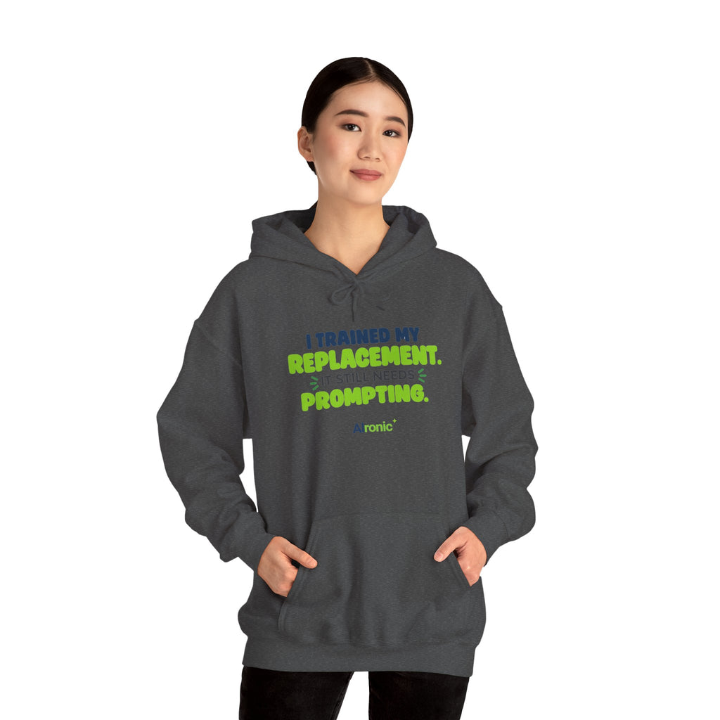 Dark Heather hoodie featuring "I trained my replacement. It still needs prompting." AIronic design, modeled front view